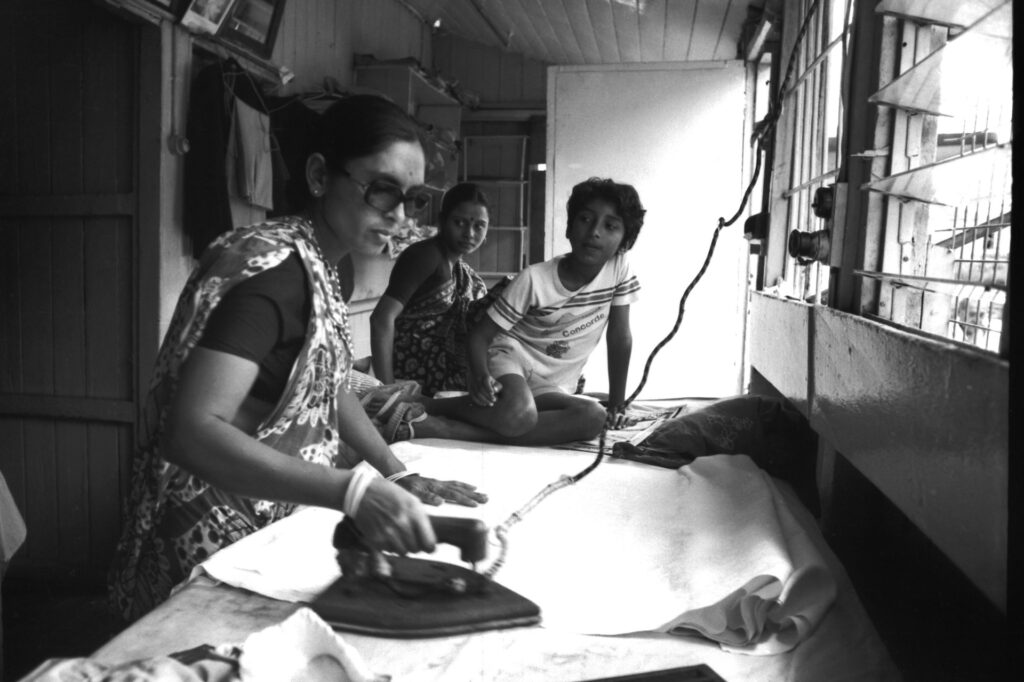 Una mujer plancha junto a dos jóvenes. Blanco y negro.