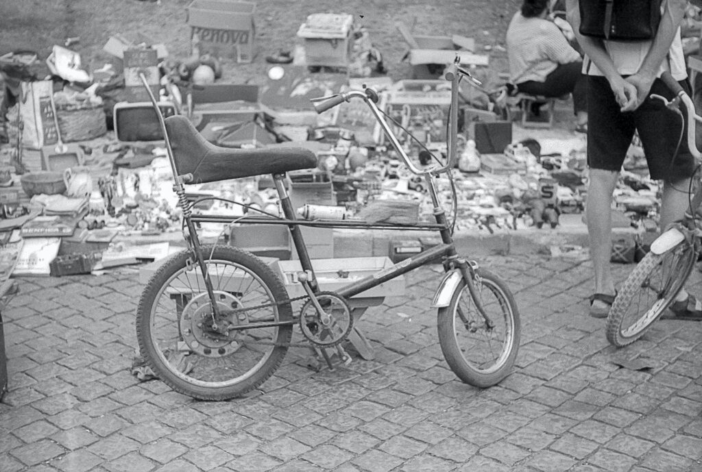 Una bicicleta abandonada delante de un mercadillo tipo rastro. Blanco y negro.