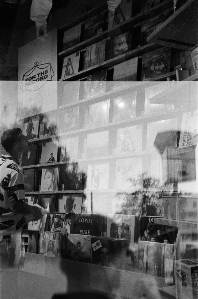 Un joven observa discos en una tienda, tras el cristal. Blanco y negro.